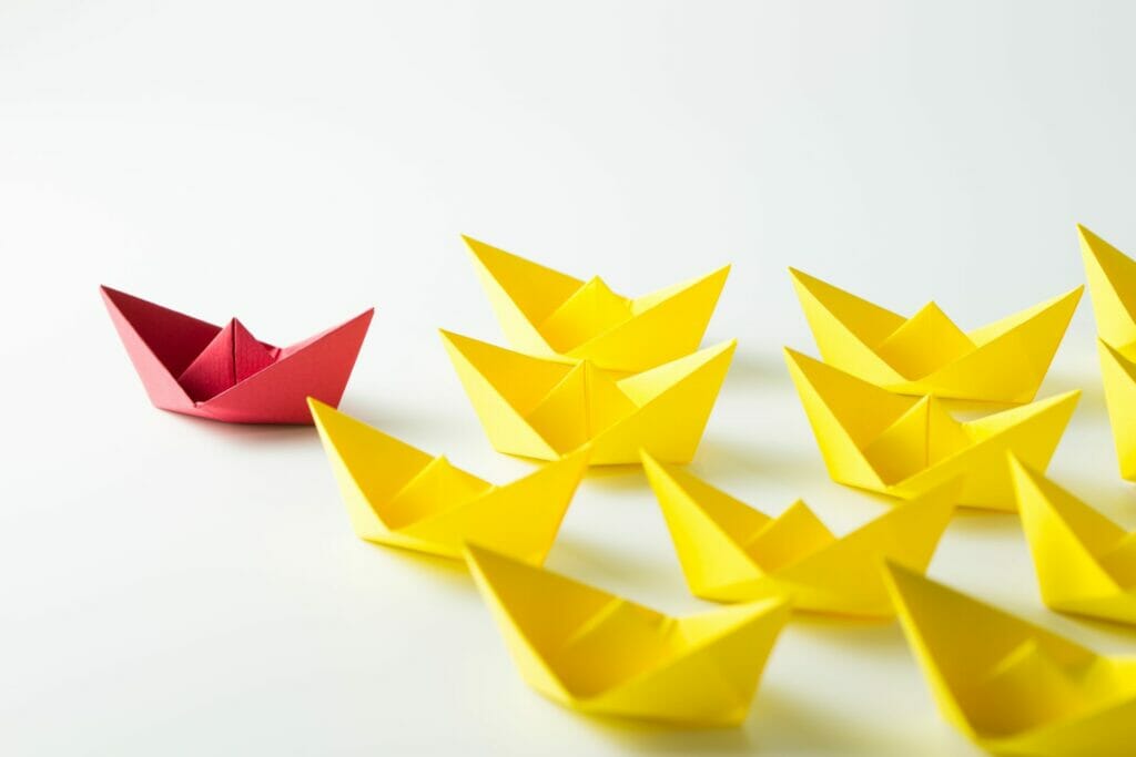Leadership concept with a red paper ship leading among yellow ships