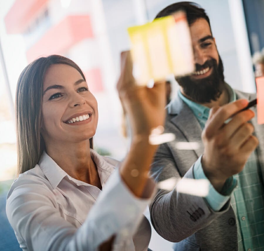 two businesspeople point to Post-It notes on glass